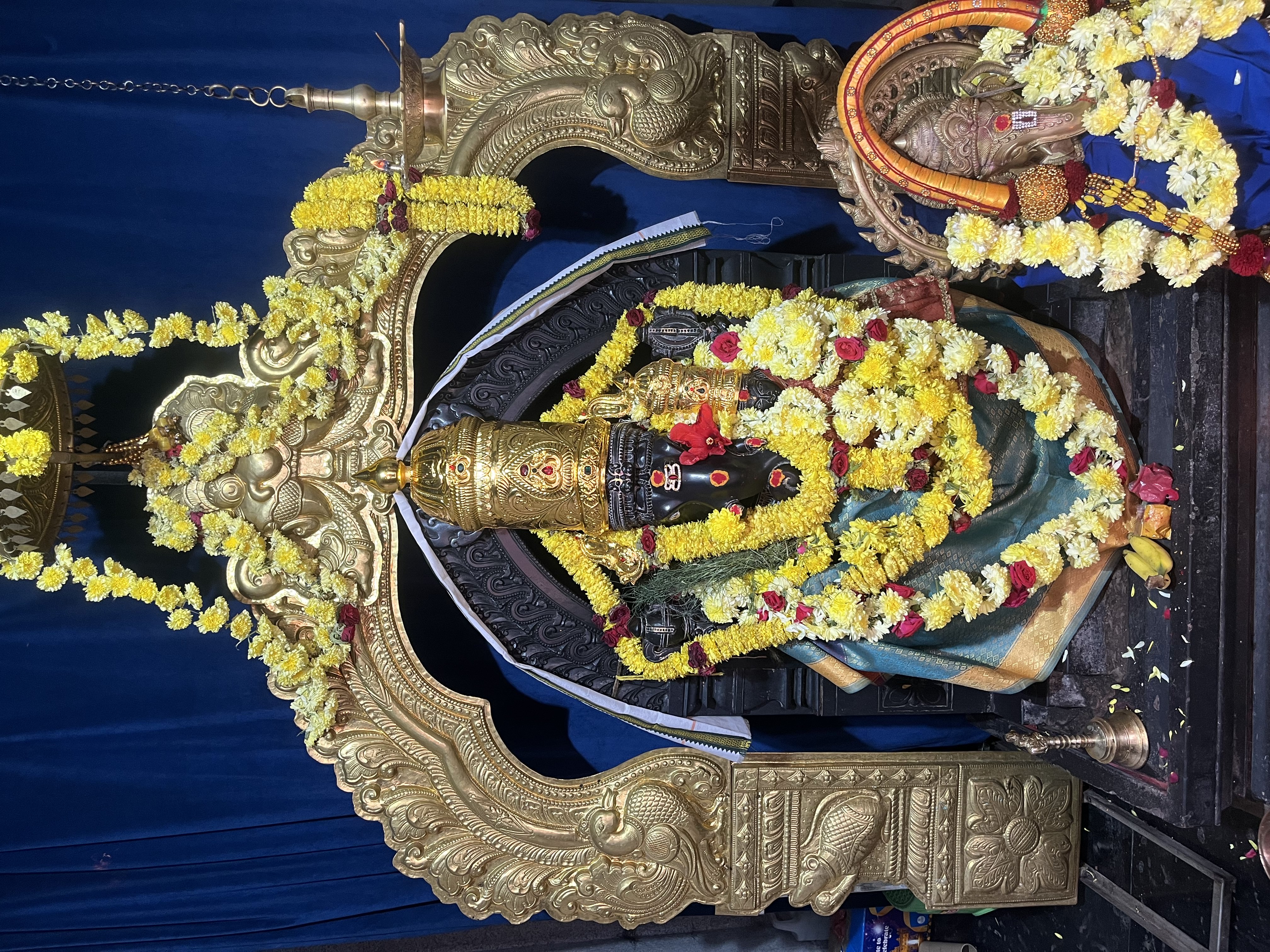 Sacred Ganesha idol adorned with golden crown, garlands of yellow and red flowers, and traditional decorations