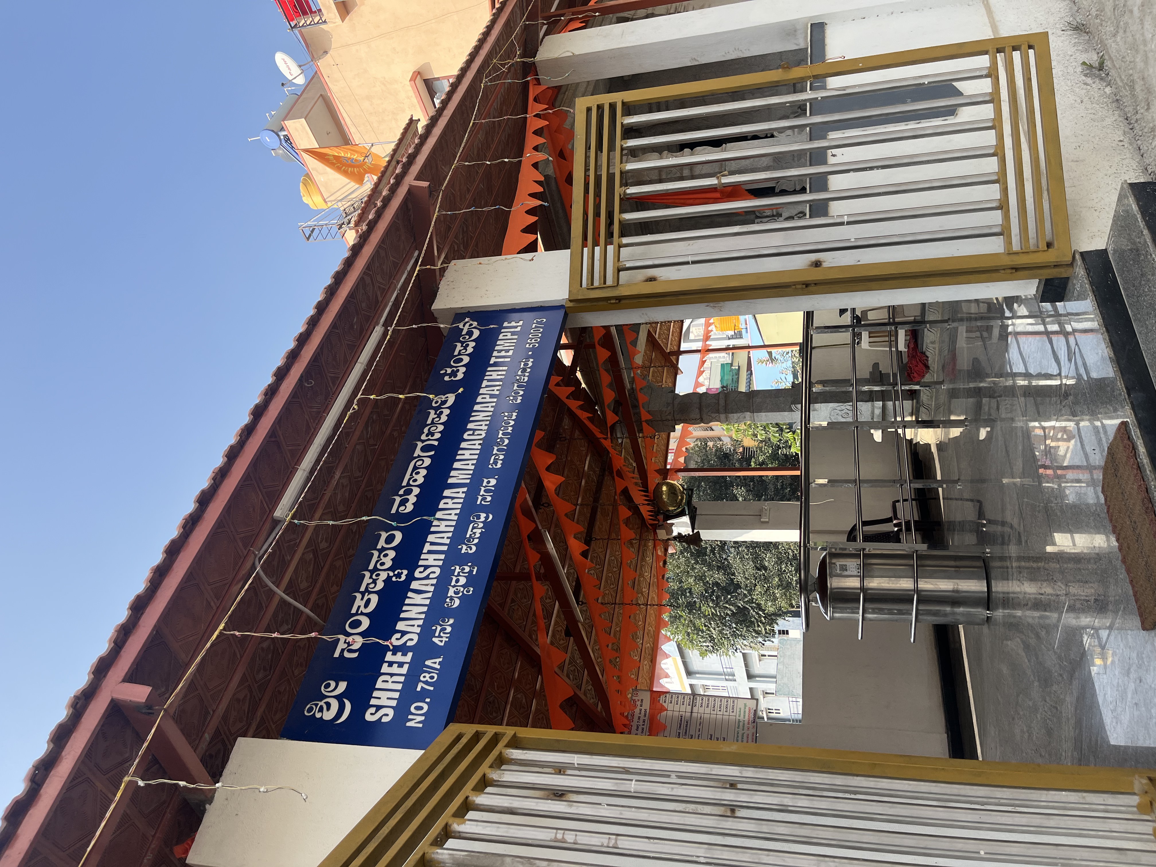 Front facade of Shri Sankashtahara Maha Ganapathi Temple showing the main entrance with blue sign, gold gates, and orange banners